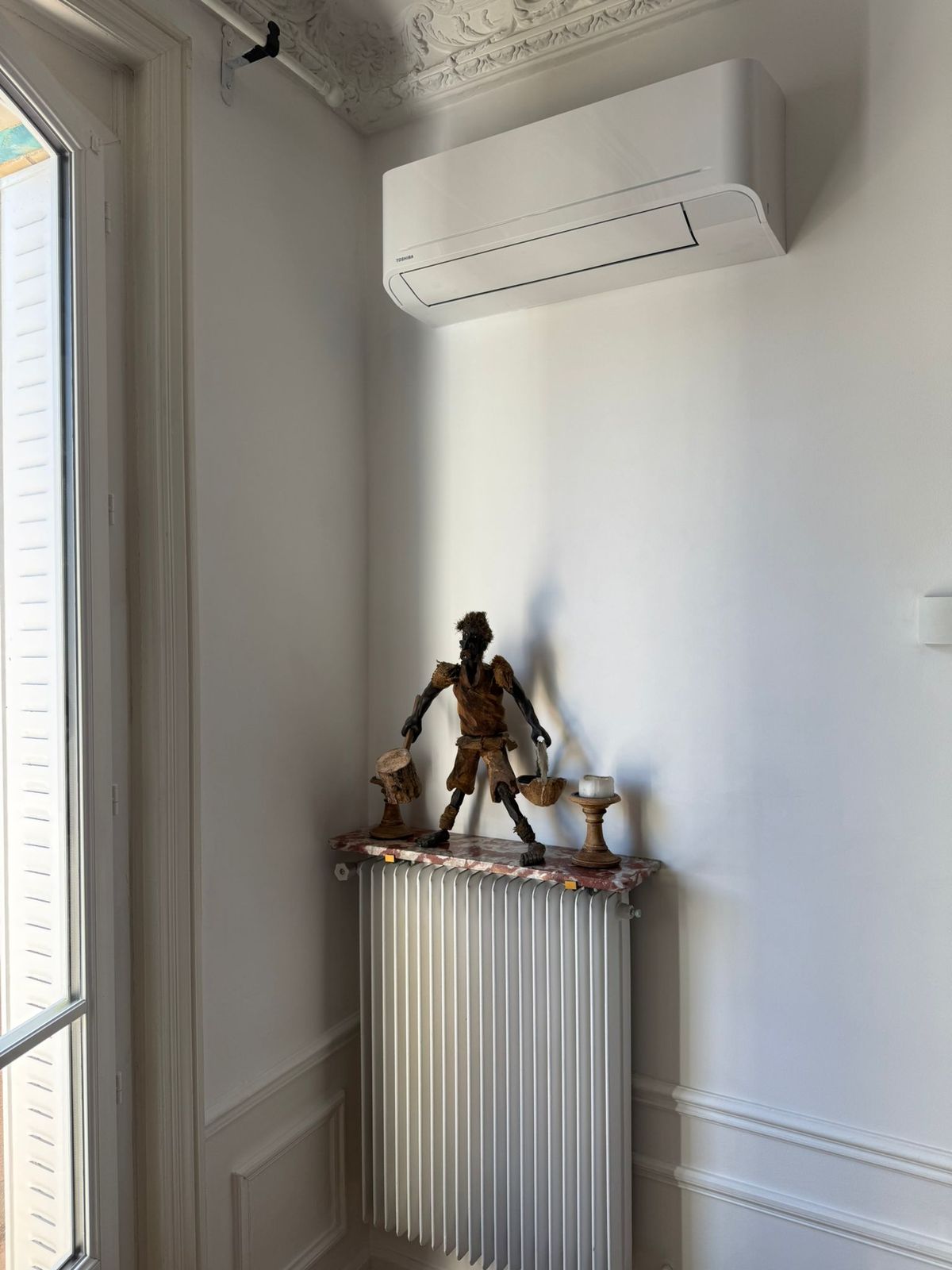 Climatiseur mural posé au-dessus d'une fenêtre, dans un appartement ancien à moulures