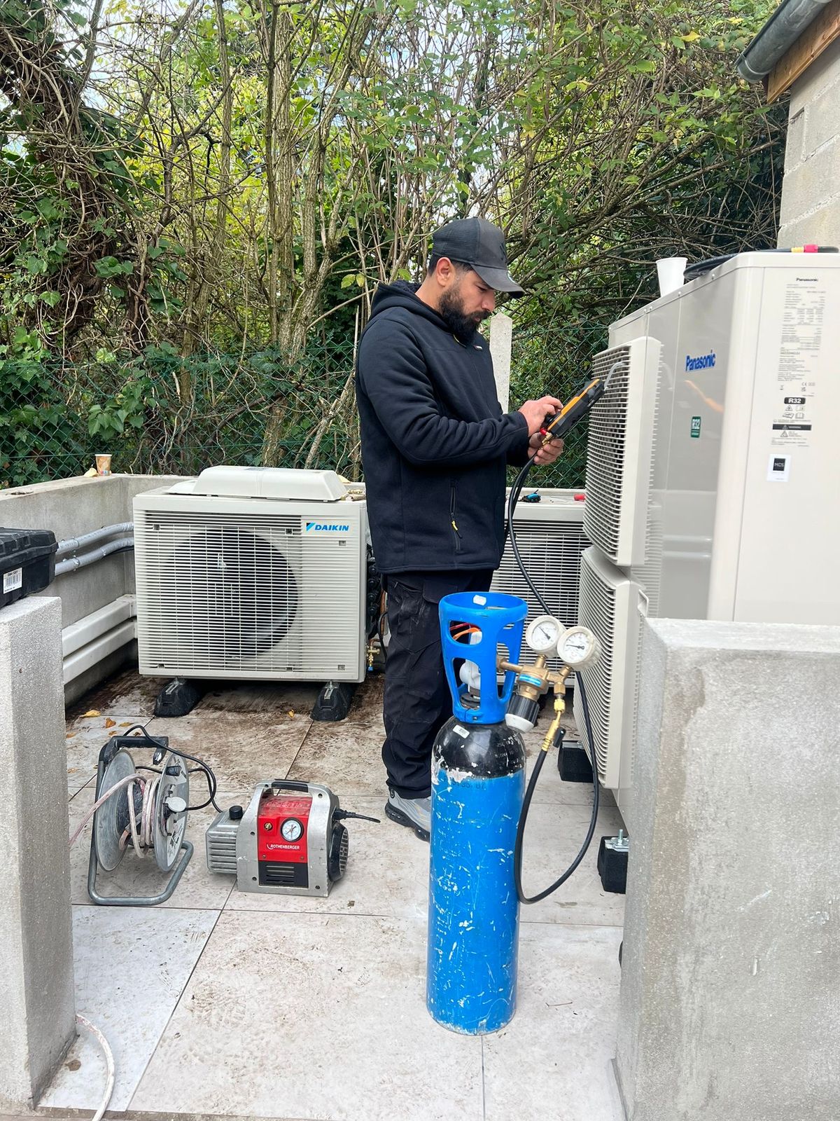 Technicien relié aux manomètres, avec bouteille d’azote et pompe à vide, devant des groupes Daikin et Panasonic